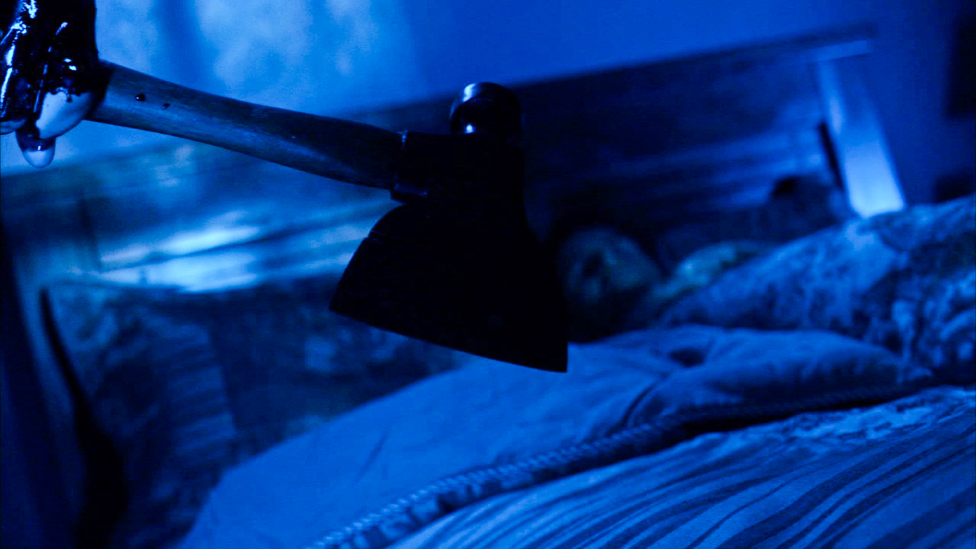 An axe swings toward a bed in cold blue light