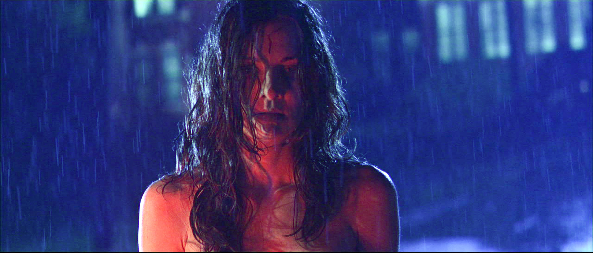 Mary stands in the rain under blue and red light