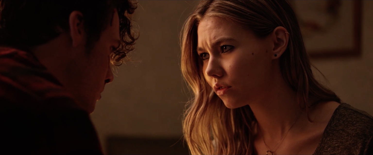 A young woman faces a young man in warm interior light