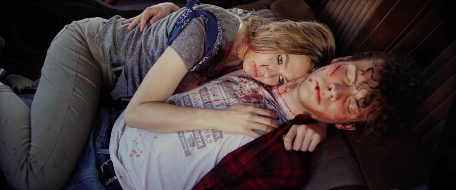 Two injured young people lie together in the back seat of a car